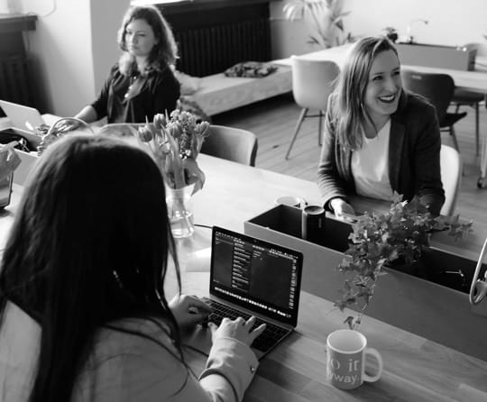 Three workers in an office, conversing and smiling.